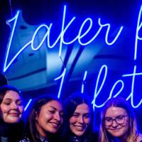 A group of grads smile and take a selfie in front of the Laker for a Lifetime sign